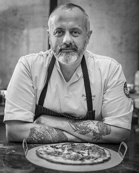 A master pizza maker having a portrait taken in front of his pizza.